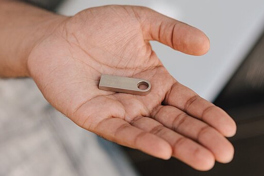 Hand mit USB-Stick und Laptop im Hintergrund